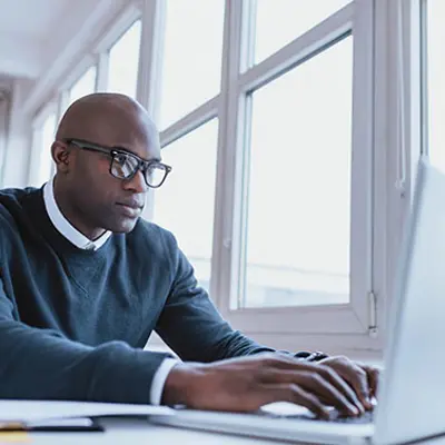 a professionally dressed man typing on a laptop at a table